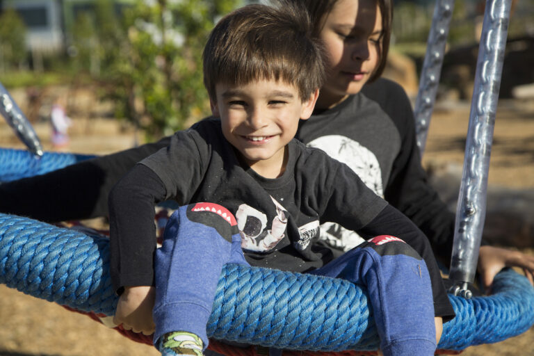 two boys play on an outdoor swing at a park